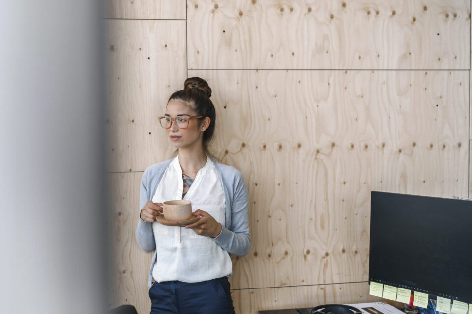 Ressourcenschonender Materialeinsatz Junge Frau arbeitet in einem modernen Büro, macht eine Pause und trinkt Kaffee aus einer Holztasse